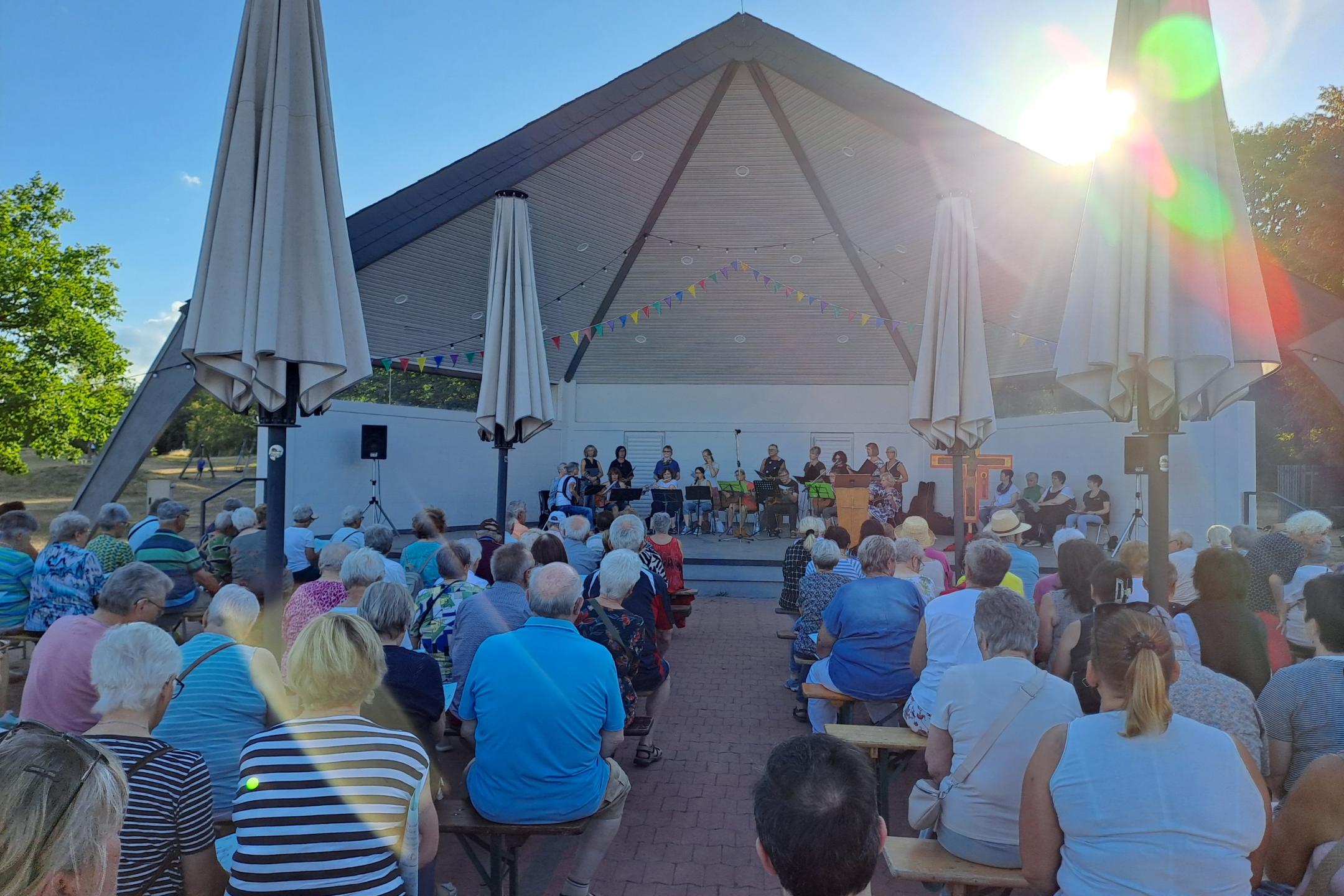 Man sieht  wie Besucher des Abendlobs mit dem mit dem Gesicht nach vorne zum Musikpavillon gerichtet am Abendlob 2026 teilnehmen. Im Hintergrund ist der Musikpavillon zu sehen.