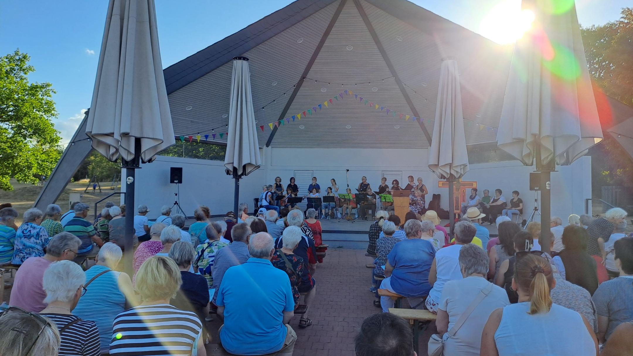 Man sieht  wie Besucher des Abendlobs mit dem mit dem Gesicht nach vorne zum Musikpavillon gerichtet am Abendlob 2026 teilnehmen. Im Hintergrund ist der Musikpavillon zu sehen.